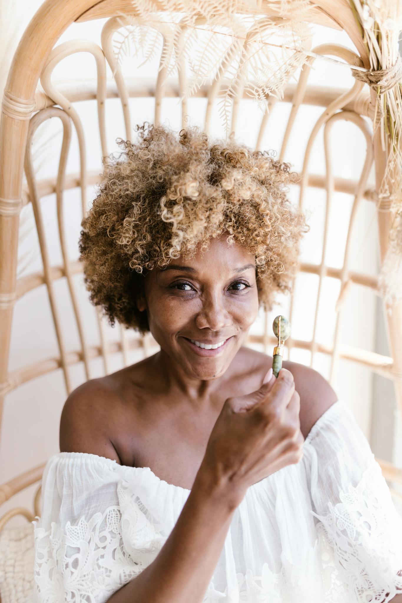 Portrait of a smiling woman with curly hair enjoying a skincare routine indoors.